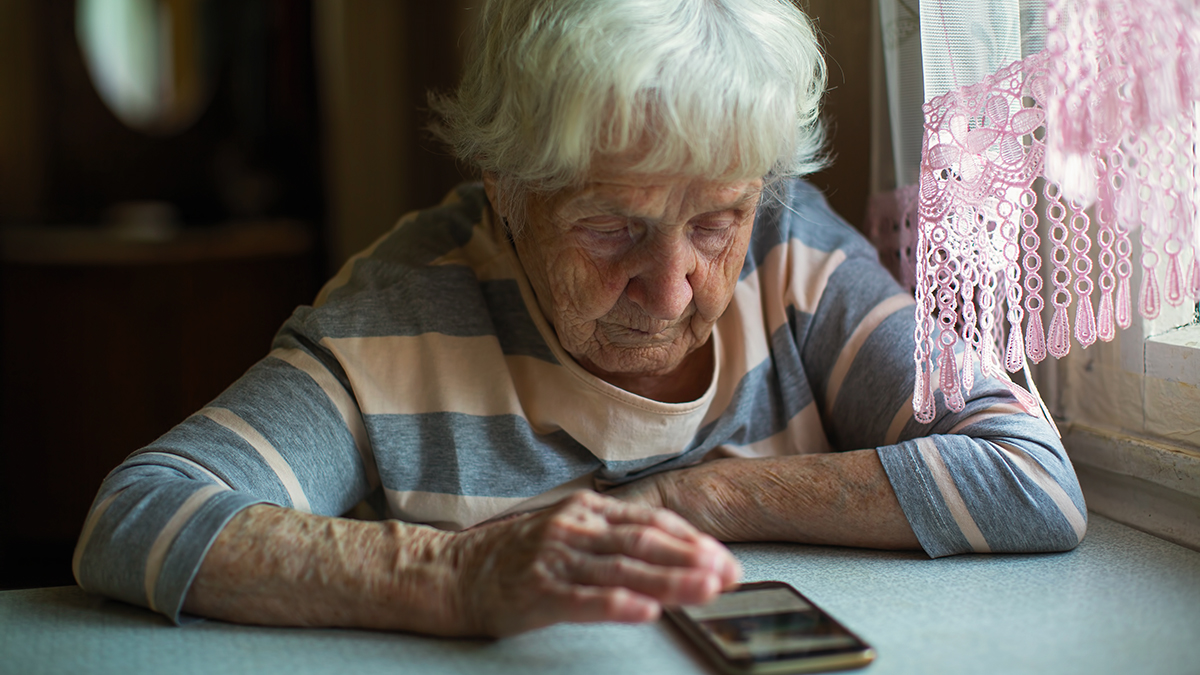 Äldre kvinna som tittar på sin mobiltelefon som ligger på bordet framför henne.