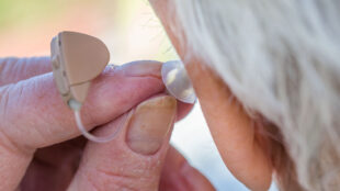 Äldre person sätter in en hörapparat i örat.