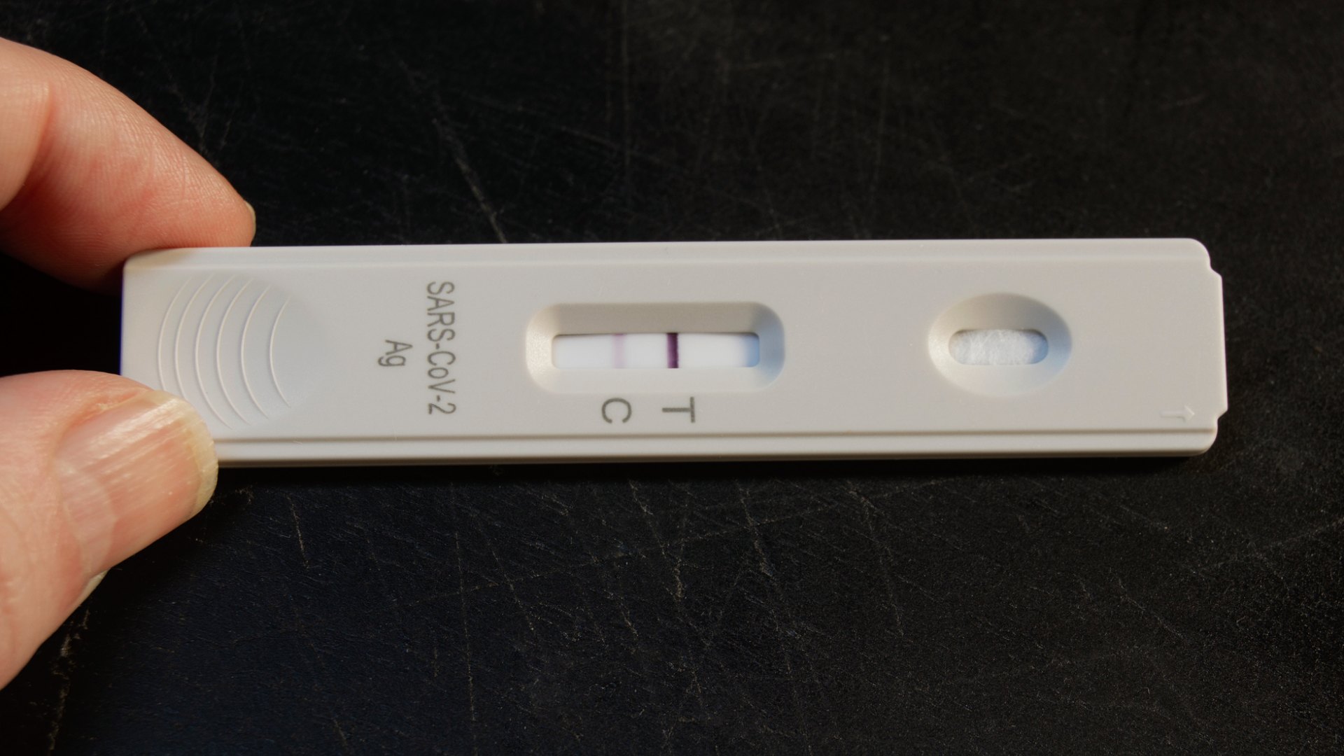 En tumme och ett pekfinger håller i ett covidtest med två streck, det vill säga positivt resultat.