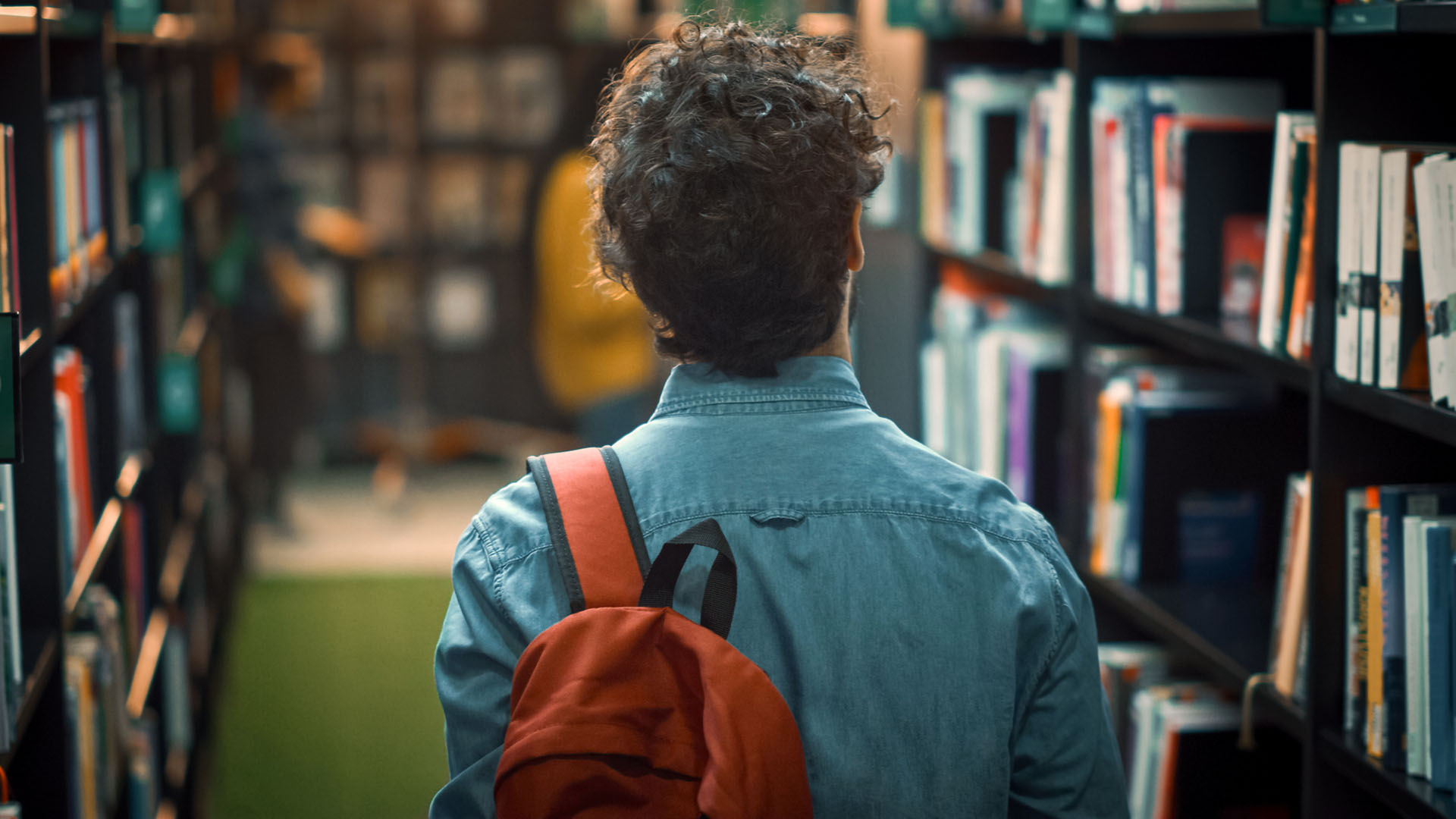 Man med ryggsäck går genom skolbibliotek.