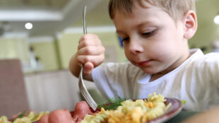 Liten pojke sätter sin gaffel i pasta och korv.