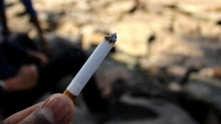 En person håller cigarett med rök mot suddig bakgrund.