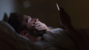 Man ligger i säng och kollar sin mobil.