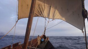 Sol varvas med skugga i seglets tyg i fören av båten.