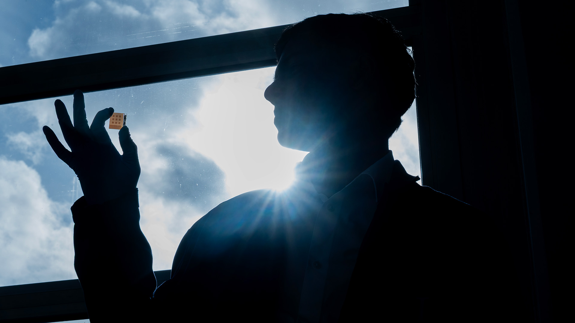 Forskaren håller upp solcell i motljus.