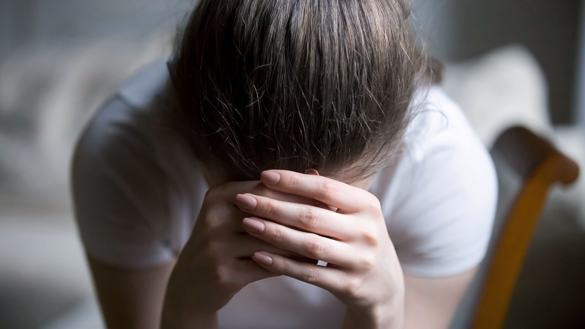 Kvinna med nedböjt huvud med händerna framför.