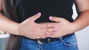 Ung kvinna håller händerna över magen.