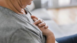 Äldre kvinna håller händerna över bröstet.