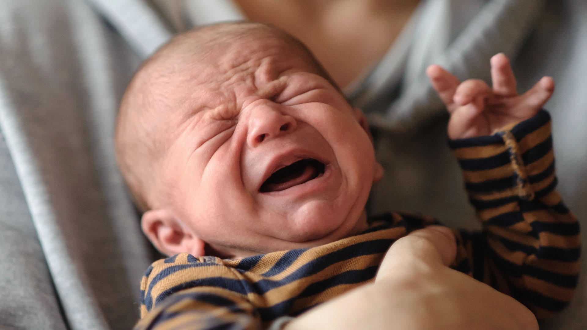 Liten pojke i randig tröja gråter i förälders famn.