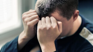 Tonårspojke håller sina händer framför ansiktet.