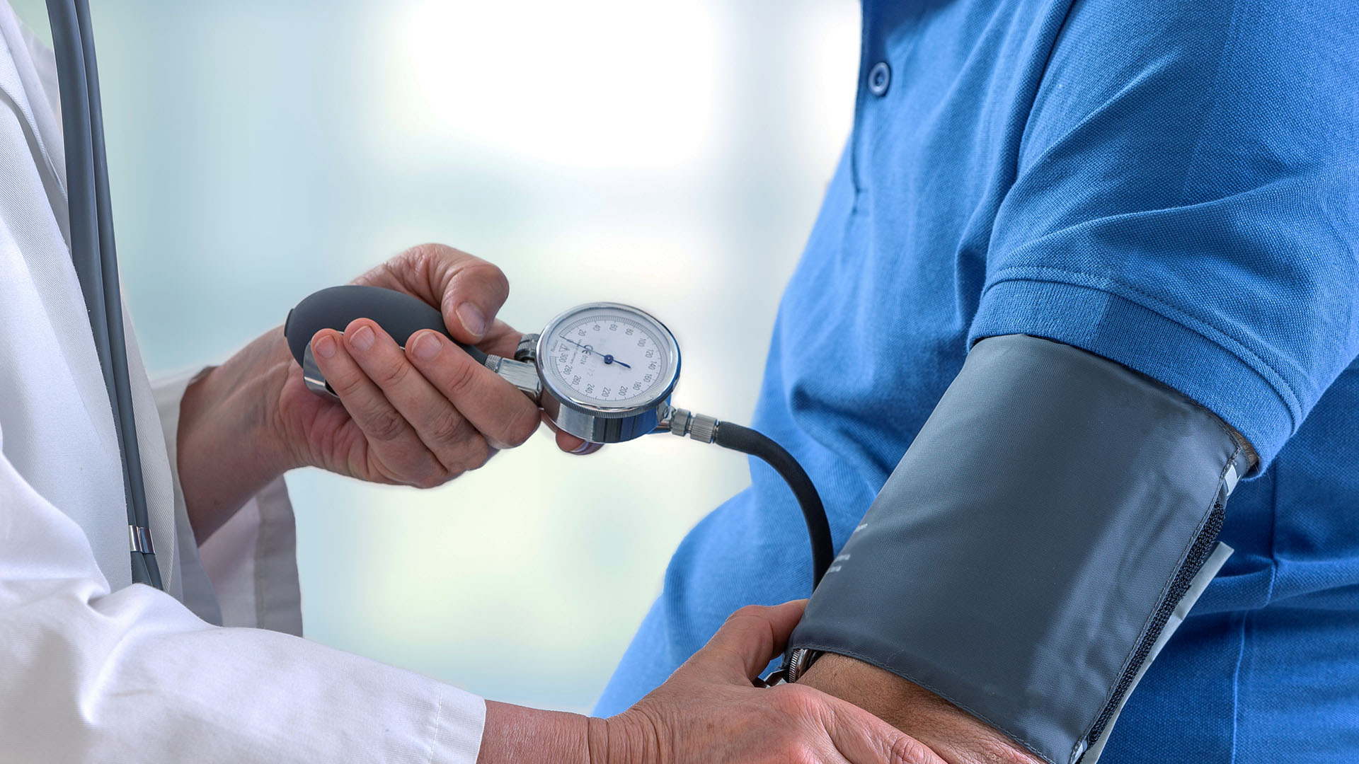 Läkare mäter blodtrycket på en patient i blå tröja.