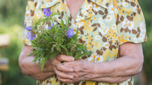 Äldre dam med en bukett blå blommor.