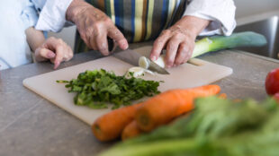 Äldre par lagar mat och skär upp grönsaker.