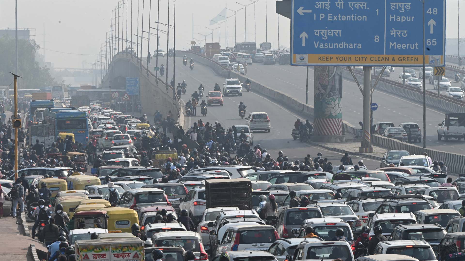 Ett myller av bilar omgivna av smog på en större väg. På en skylt står "Keep your city clean and green"