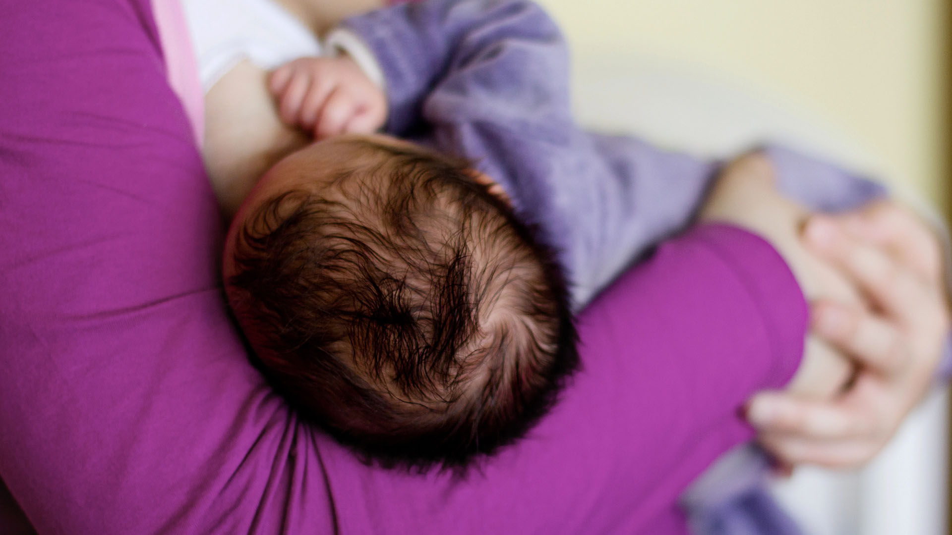 Bebis med mörkt hår ammas.