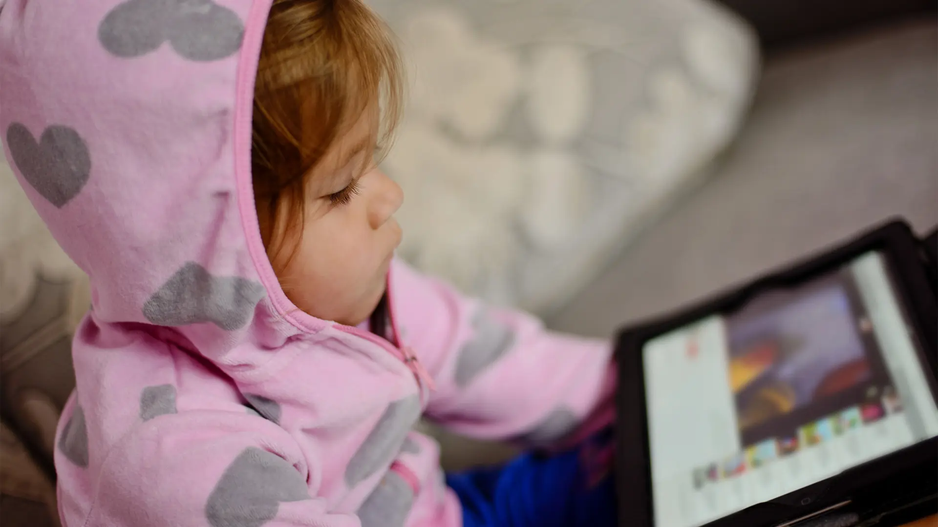 Flicka i rosa jacka med luva tittar på en skärm.