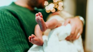 Pappa i grön tröja håller sin nyfödda bebis i famnen.