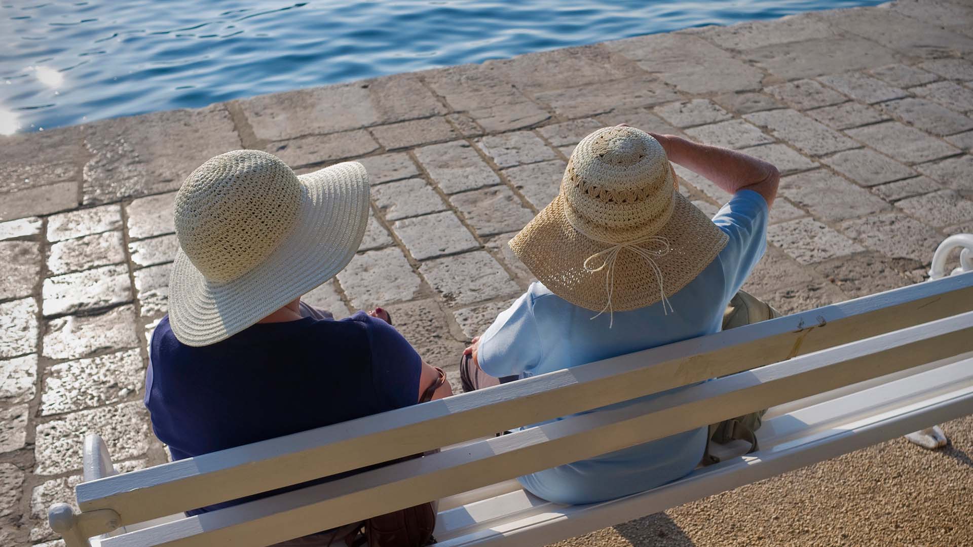 Två damer sitter på en bänk med stora solhattar.