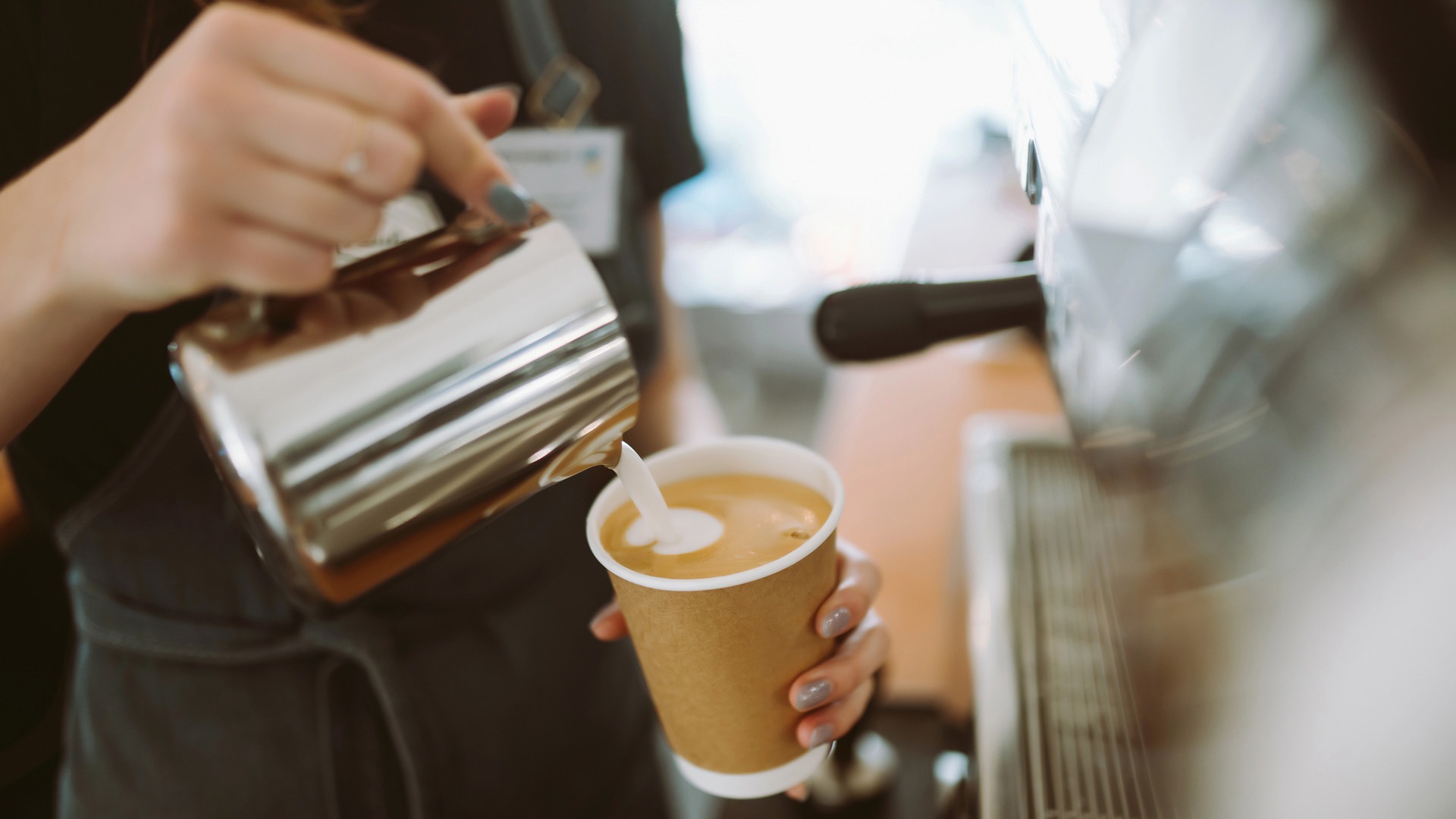 Ung kvinna häller skummad mjölk i en kopp vid en expressomaskin.