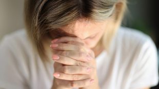 Kvinna med rosa nagellack håller händerna framför ansiktet.