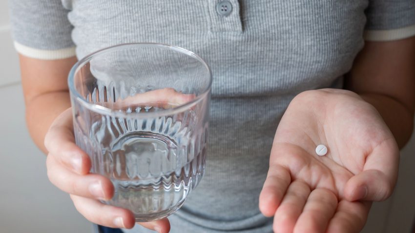 Barn i grå tröja håller en tablett i ena handen och ett glas i den andra.