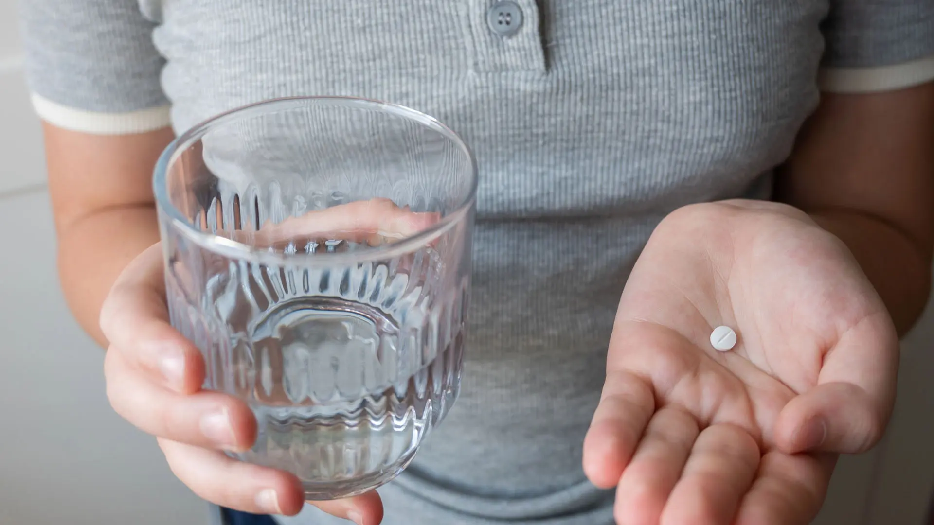 Barn i grå tröja håller en tablett i ena handen och ett glas i den andra.
