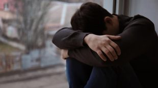 Man sitter intill fönster och gömmer sitt ansikte.