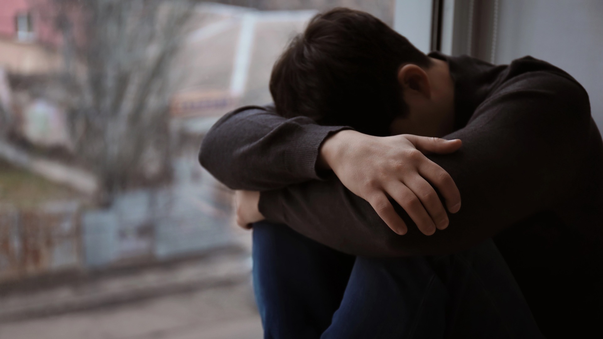 Man sitter intill fönster och gömmer sitt ansikte.