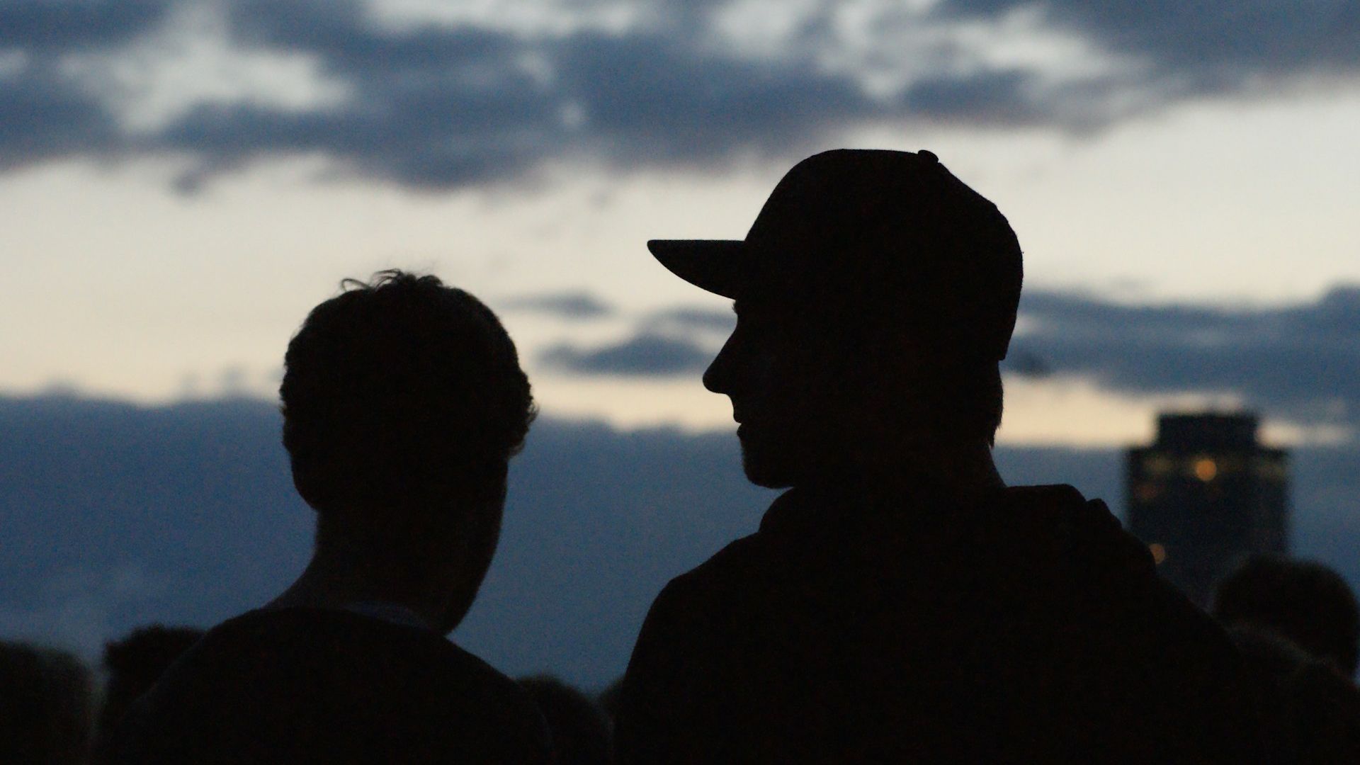 Två unga män, den ena i keps, i svart siluett mot kvällshimmel.