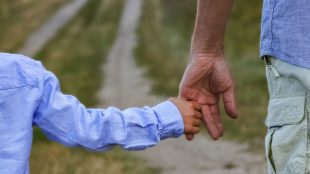 Landsväg, ett barn i ljusblå skjorta håller en vuxen man i handen.