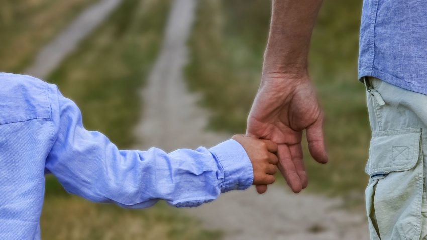 Landsväg, ett barn i ljusblå skjorta håller en vuxen man i handen.