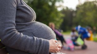 Kvinna med stor mage sitter på en bänk utomhus.