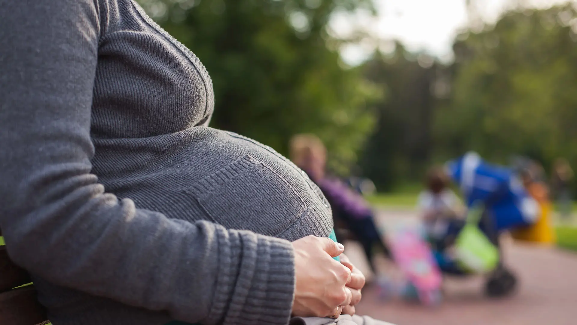 Kvinna med stor mage sitter på en bänk utomhus.