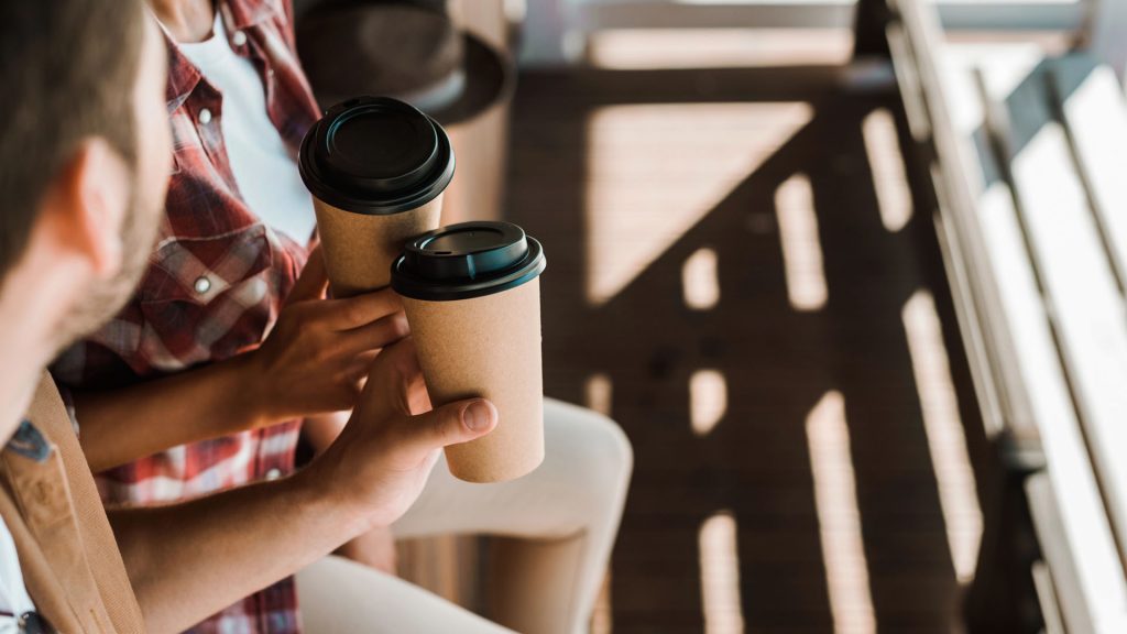 Två personer håller i varsin pappersmugg med kaffe.