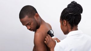 Kvinna i vit rock undersöker ryggen på en man med ett förstoringsglas.