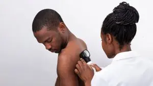 Kvinna i vit rock undersöker ryggen på en man med ett förstoringsglas.