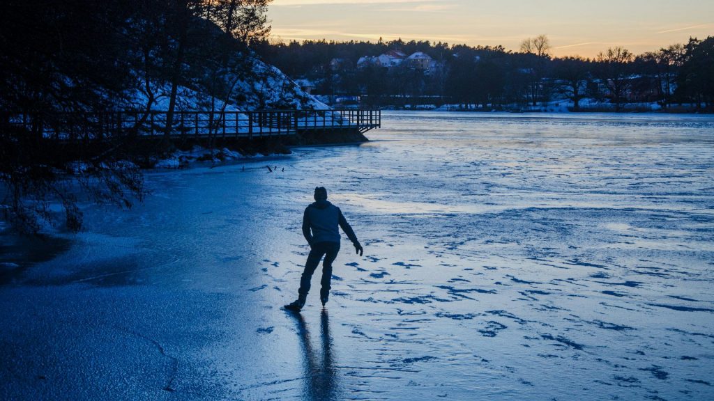 Person, i svart siluett, åker skridskor på is på en sjö.