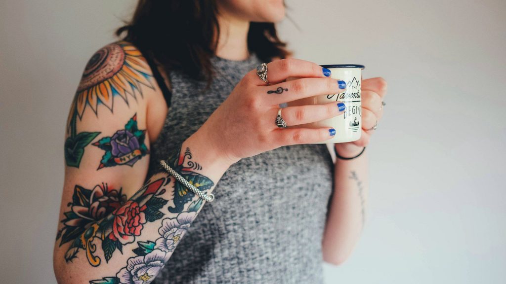 Kvinna med tatuerad arm håller i tekopp.