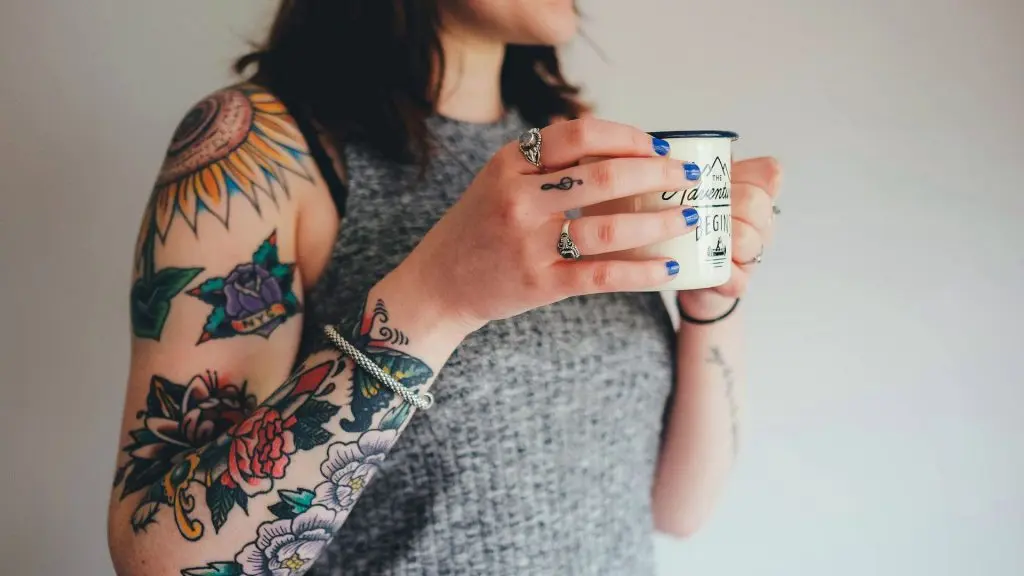 Kvinna med tatuerad arm håller i tekopp.