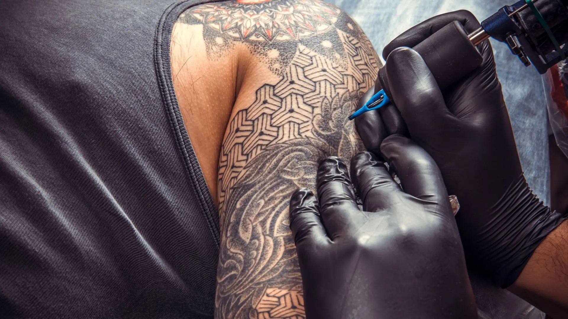 Man får armen tatuerad. Två händer med svarta handskar tatuerar med nål.