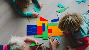 Tre barn i lågstadieåldern leker med pussel på ett ljust trägolv.