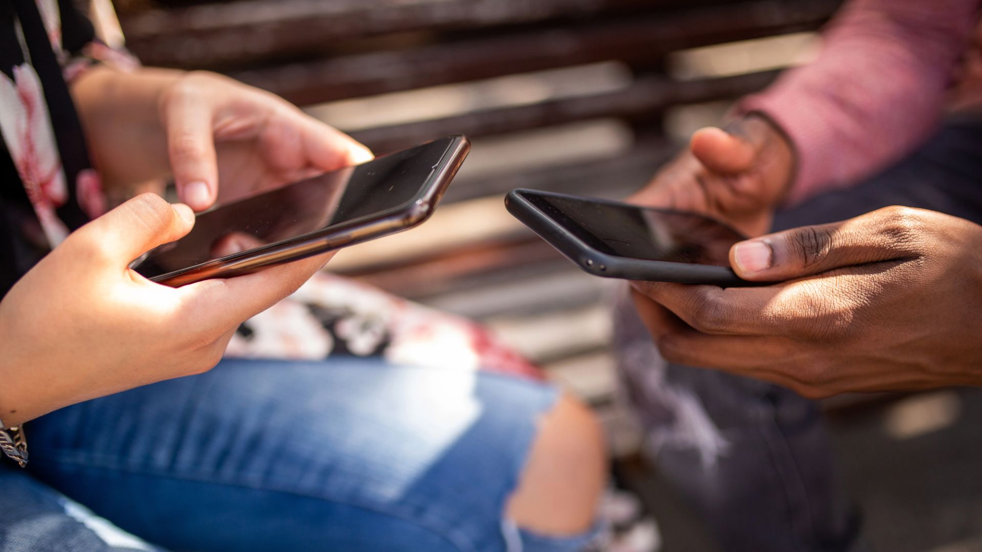 Bara händer syns på två personer som sitter mittemot varandra med varsin telefon i handen.