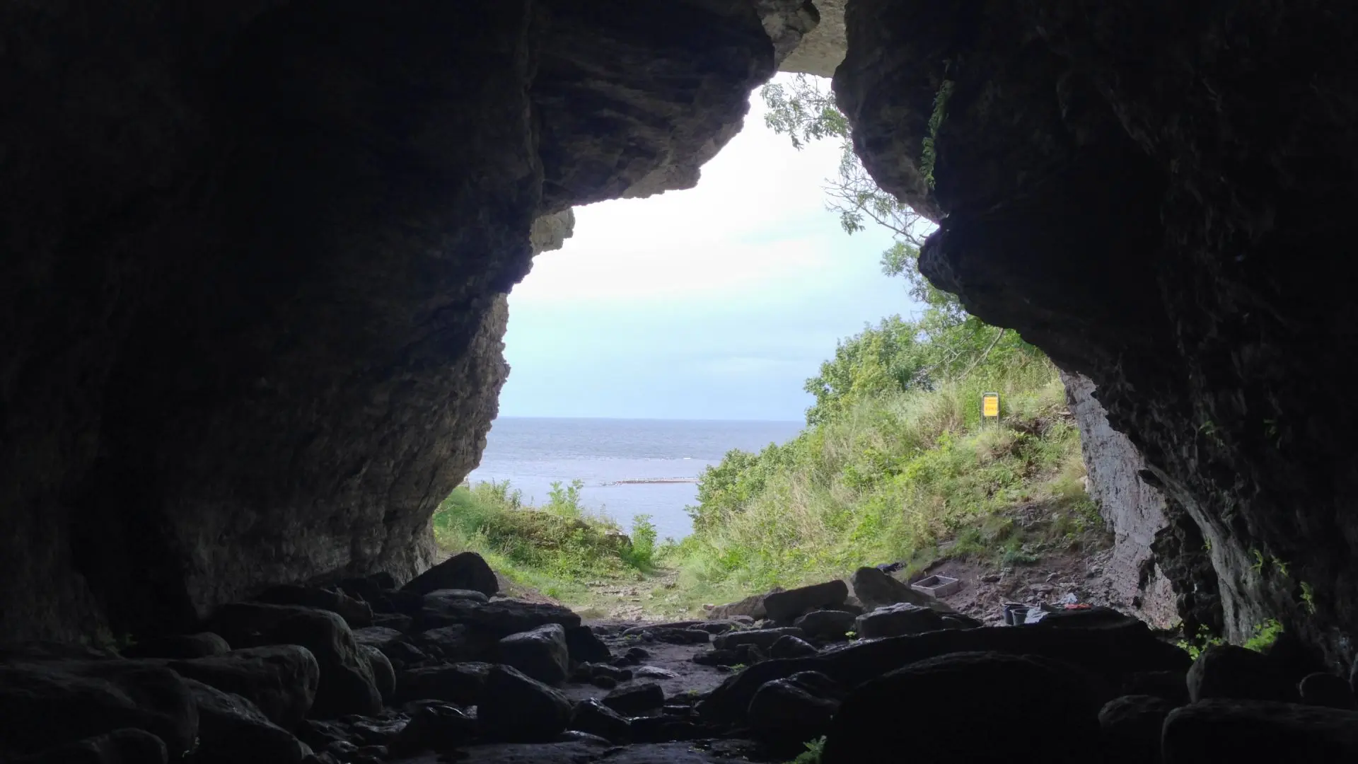 Stor grotta sedd inifrån. Grönska och hav utanför.