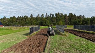 En åker med en traktor samt rader av solpaneler som står vertikalt mot marken.