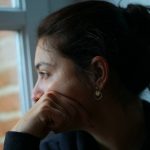 Tankfull kvinna med mörkt hår i en tofs tittar ut genom ett fönster.