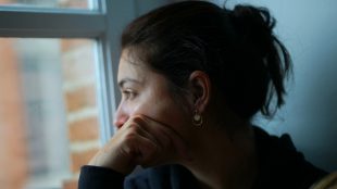 Tankfull kvinna med mörkt hår i en tofs tittar ut genom ett fönster.