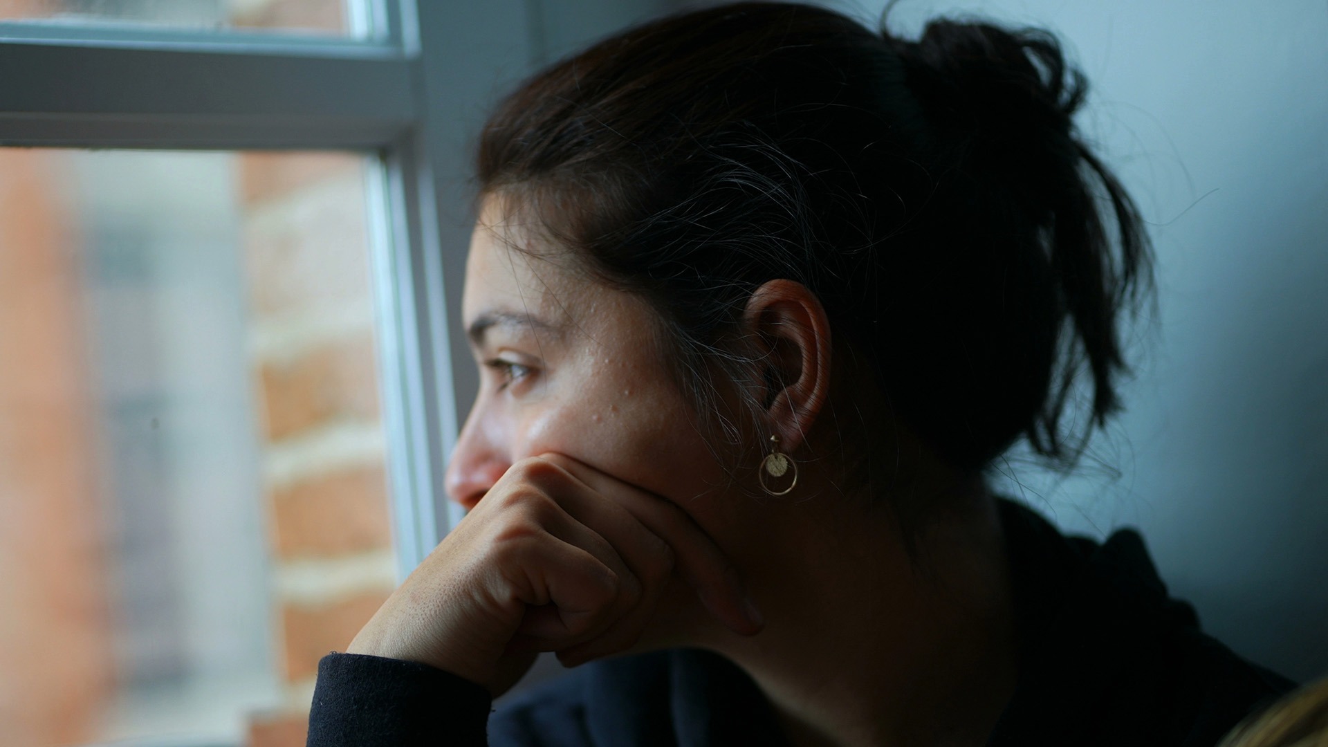 Tankfull kvinna med mörkt hår i en tofs tittar ut genom ett fönster.