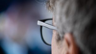 Man med grått hår och glasögon tittar mot en suddig skärm.