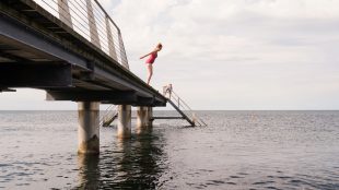 Kvinna i baddräkt, på väg att hoppa i vattnet från en pir.