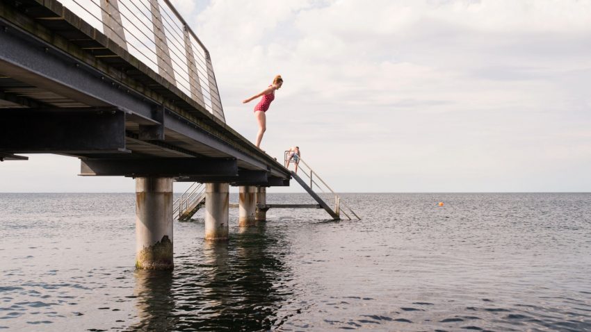 Kvinna i baddräkt, på väg att hoppa i vattnet från en pir.